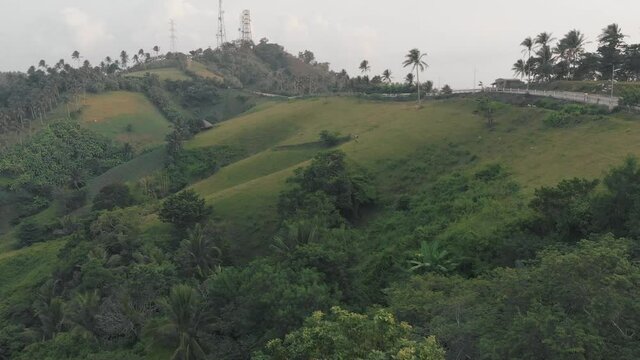 Green tropical hills and the road surrounded by palms. Camalig Albay, Philippines aerial cinematic shot