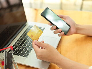 Man hands holding smartphone and credit card on wooden table with laptop