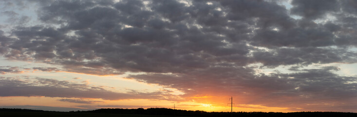 Fototapeta na wymiar Panorama of sunset over dark forest. Electric poles on a background of bright orange sun sky.