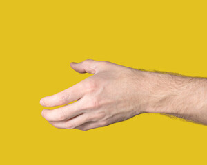 Close-up of outstretched male hand with open palm ready to shake other hand on yellow background....