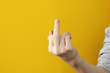 hand of teenager shows middle finger on yellow background. Fuck off