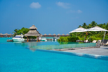 Scenic  landscape of Maldives beach and pier with speed boats and yachts on the horizon. Seascape with water bungalows, beautiful turquoise sea and lagoon waters, tropical nature paradise. 