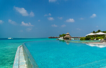 Scenic  landscape of Maldives beach and pier with speed boats and yachts on the horizon. Seascape with water bungalows, beautiful turquoise sea and lagoon waters, tropical nature paradise. 