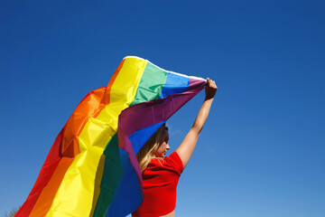 girl with lgbt flag behind her back against a bright blue sky