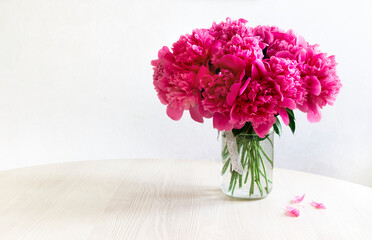 there is a transparent glass vase with a large bouquet of pink peonies on a light wooden table. copy space