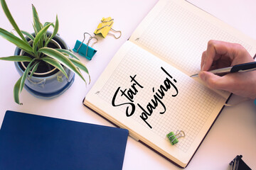 Closeup of a personal agenda setting an important date writing with pen. The words Start Playing written on a white notebook to remind you an important appointment.