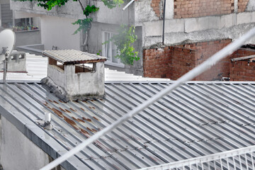 Rainy day and wet roof of house made of metal panels. Corrosion exists on roof and old style chimney stack during overcast weather.