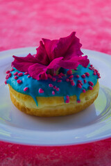 Donut with blue glaze and pink flower on pink background close up vertically