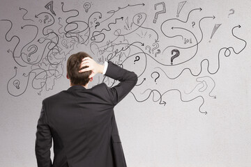 Stressed businessman with abstract arrows sketch on concrete wall background. Confusion and...