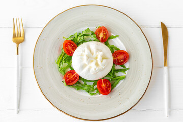 Salad with burrata cheese and cherry tomatoes on white wooden background