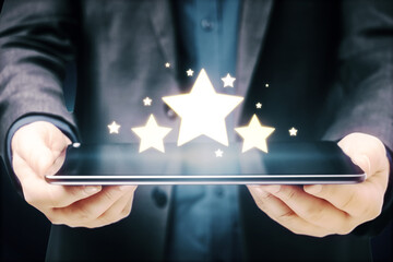 Businessman hands holding tablet with glowing stars on blue background. Customer feedback and...