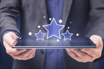 Businessman hands holding pad with glowing stars on blue background. Customer feedback and online ranking concept.