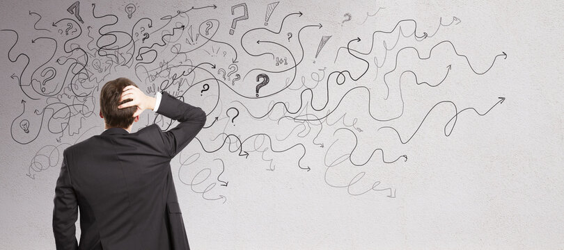 Pensive businessman with abstract arrows sketch on concrete wall background. Confusion and direction concept.