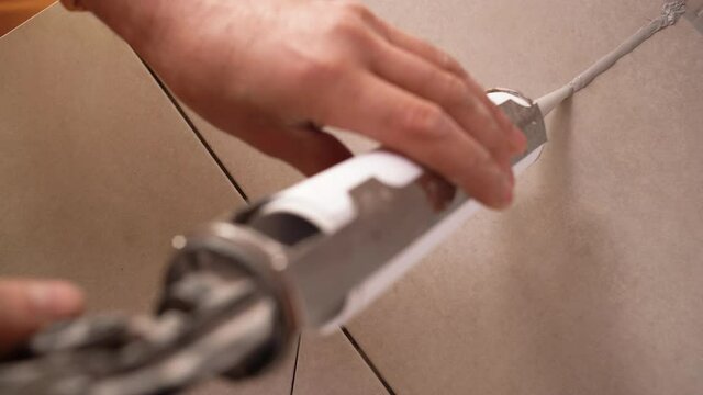 Close-up image of applying silicone sealant with a sealing gun, male hands apply silicone adhesive on the floor to ceramic tiles in the bathroom. Service concept.