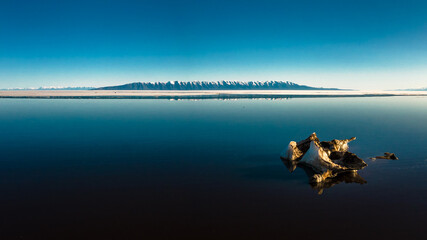 Naklejka premium minimalistic view of seascape with melting ice on foreground and mountain range on background with blue sky reflected in water at daylight