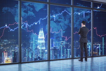 Businessman standing in modern office interior with forex chart and night city view. Occupation and trade concept.