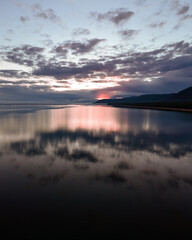 colourful view of seascape with melting ice on foreground and mountain range on background with cloudy sky reflected in water at sunset sunrise