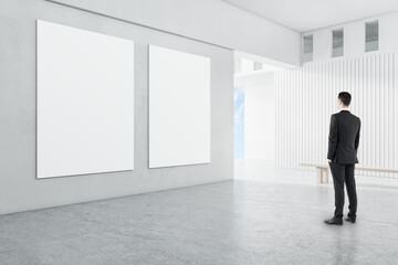 Man in modern concrete interior with empty frames looking at mockup place for your advertisement.