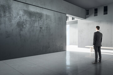 Businessperson in modern concrete interior with empty wall looking at mockup place for your advertisement.