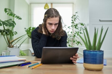 Online lesson, guy student teenager studying at home remotely using digital tablet