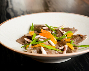 Buckwheat dumplings with fresh mushrooms served on a white plate over black background.