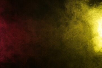 Artificial magic smoke in red-yellow light on black background