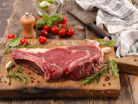 raw ribeye beef steak with herbs on wooden board