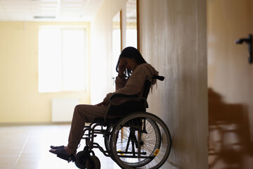 Fototapeta na wymiar Sad woman disabled sitting in wheelchair and holding her head in clinic