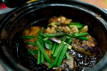 Close up Vietnamese Fish simmered with Caramel Sauce. Delicious Vietnamese clay pot fish with sauce, onion, greaves,chilies and herbs