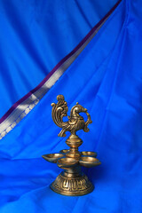 Indian traditional bronze oil lamp in the form of a bird on a blue sari background. Metal diya....