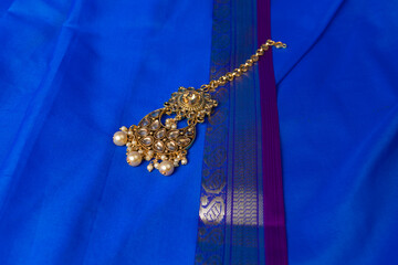 Indian traditional gold Indian wedding women's jewelry tikka on blue saree background. Close-up....