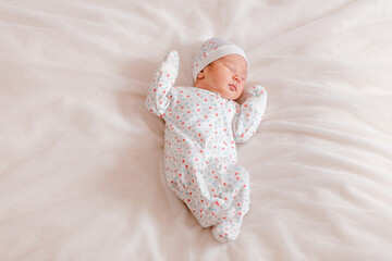 newborn baby in cap and overalls is sweet sleeping on a white sheet. one week from birth