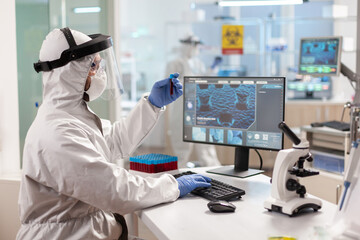 Scientist dressed in ppe suit working on computer holding vaccutainer. Medical team examining vaccine evolution in medical lab using high tech and chemistry tools for scientific research