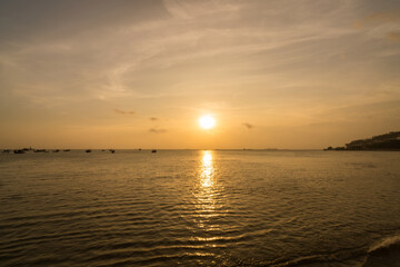 Obraz premium Beautiful sunset tropical beach with small boat and pink sky and ocean waves on a tropical sea at Vung Tau. Tropical Seascape with a boat on sandy beach at cloudy sunrise or sunset.