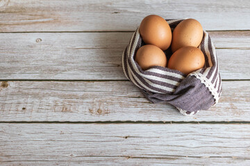 Brown chicken eggs lay on the wooden floor with brown fabric.