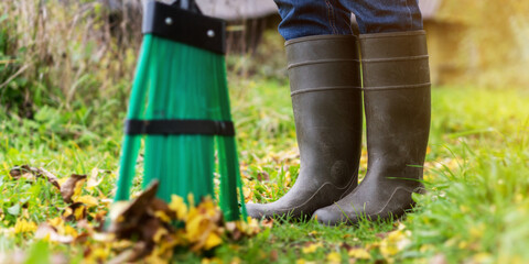 Worker with broom sweeps lawn from fallen leaves in autumn season. - obrazy, fototapety, plakaty