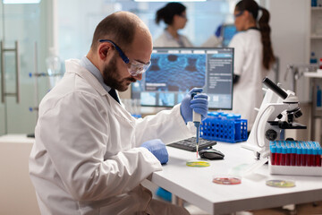 Pharmaceutical scientist dropping blood sample using micropipette on petri dish. Team of...