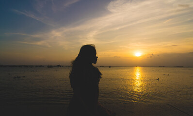 Back view silhouette young girl asian with depressed pose on the beach at sunset. Beautiful blonde woman with long hair depressing at the ocean. Concept of depress, sad