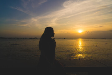 Back view silhouette young girl asian with depressed pose on the beach at sunset. Beautiful blonde woman with long hair depressing at the ocean. Concept of depress, sad