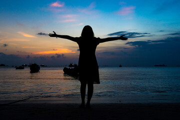 Fototapeta premium Back view silhouette young girl asian with happy and peacful pose on the beach at sunset. Beautiful blonde woman with long hair relaxing at the ocean. Concept of happy, peaceful, relax