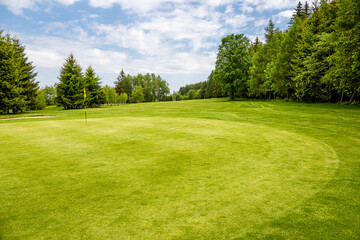 Golf green with flag in spring nature under blue sky