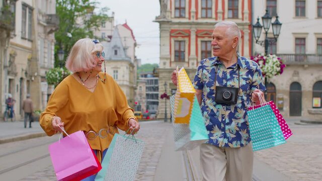 Senior old stylish tourists man woman walks with colorful bags after shopping in mall. Elderly grandmother, grandfather having good time, traveling together on city street Lviv, Ukraine. Mature family