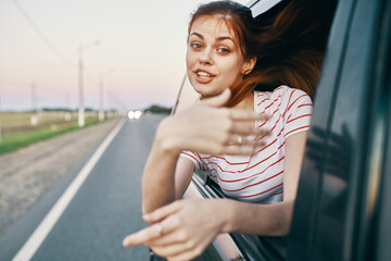 red-haired woman in a t-shirt looks out of the car window and gestures with her hands on the summer road