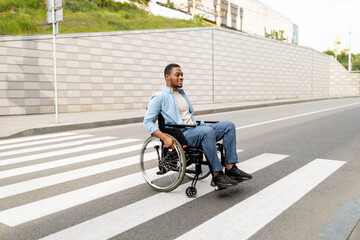Full length portrait of impaired young black guy in wheelchair crossing city street, copy space
