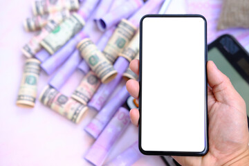 Hand holding smartphone with money on the table and work space, business and technology concept