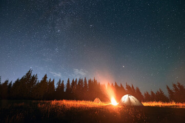 Wide angle view on beautiful landscape in the mountains. Two tents, one glowing, and campfire under...