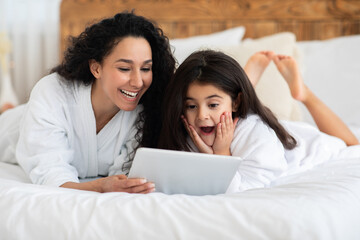 Emotional mom and little girl laying on bed with pad