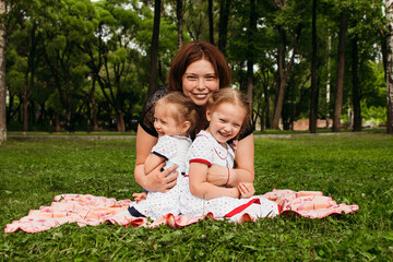 Mom hugs her daughters in the fresh air. European appearance woman tickles two girls active games...