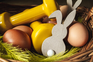 Traditional Easter wicker basket with eggs, decorative bunny and yellow dumbbells. Easter fitness...