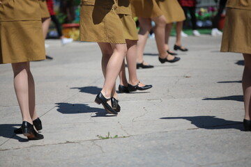 Image of a group of female legs in black shoes and a short soldier's skirt dancing a step at an open-air parade in the square on a summer day.Woman dancer in camouflage clothes.Background